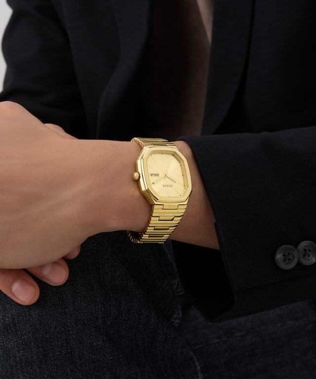 GUESS Mens Gold Tone Date Watch on a person's wrist with a dark suit background