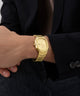GUESS Mens Gold Tone Date Watch on a person's wrist with a dark suit background