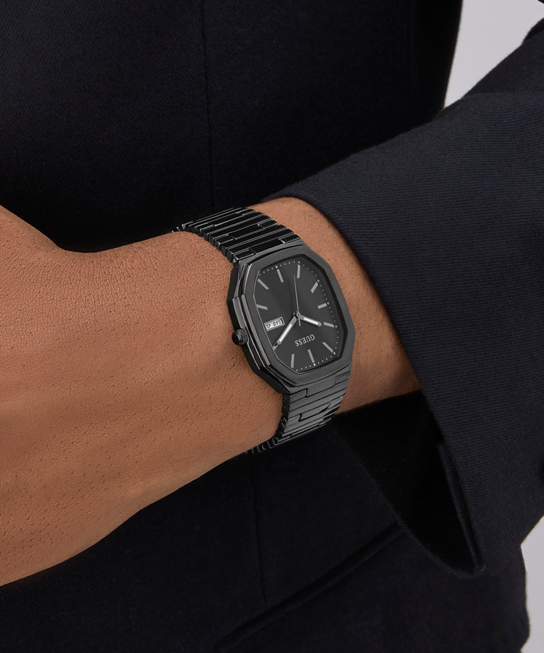 GUESS Mens Black Date Watch on a person's wrist with a blurred background