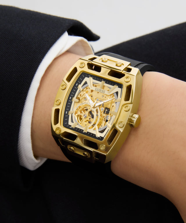GUESS Mens Black Gold Tone Automatic Watch with visible brand logo on a person's wrist against a neutral background