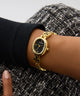 GUESS Ladies Gold Tone Analog Watch on a wrist with a textured black and white background
