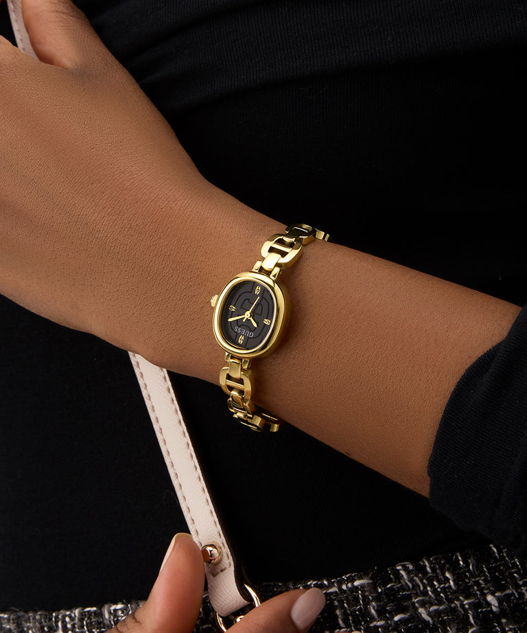 Gold GUESS Ladies Gold Tone Analog Watch on a person's wrist with a dark background