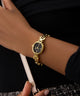 Gold GUESS Ladies Gold Tone Analog Watch on a person's wrist with a dark background
