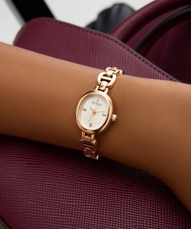GUESS Ladies Rose Gold Tone Analog Watch on a wrist with a maroon background