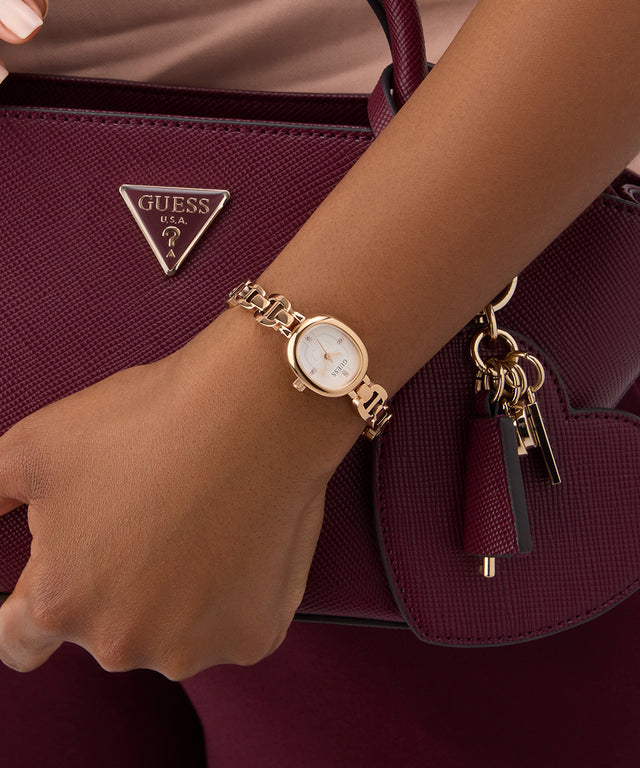 GUESS Ladies Rose Gold Tone Analog Watch on a wrist with a maroon handbag featuring a Guess logo.