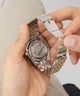 Close-up of a hand holding a GUESS Mens 2-Tone Automatic Watch with a visible brand logo and inner mechansim.