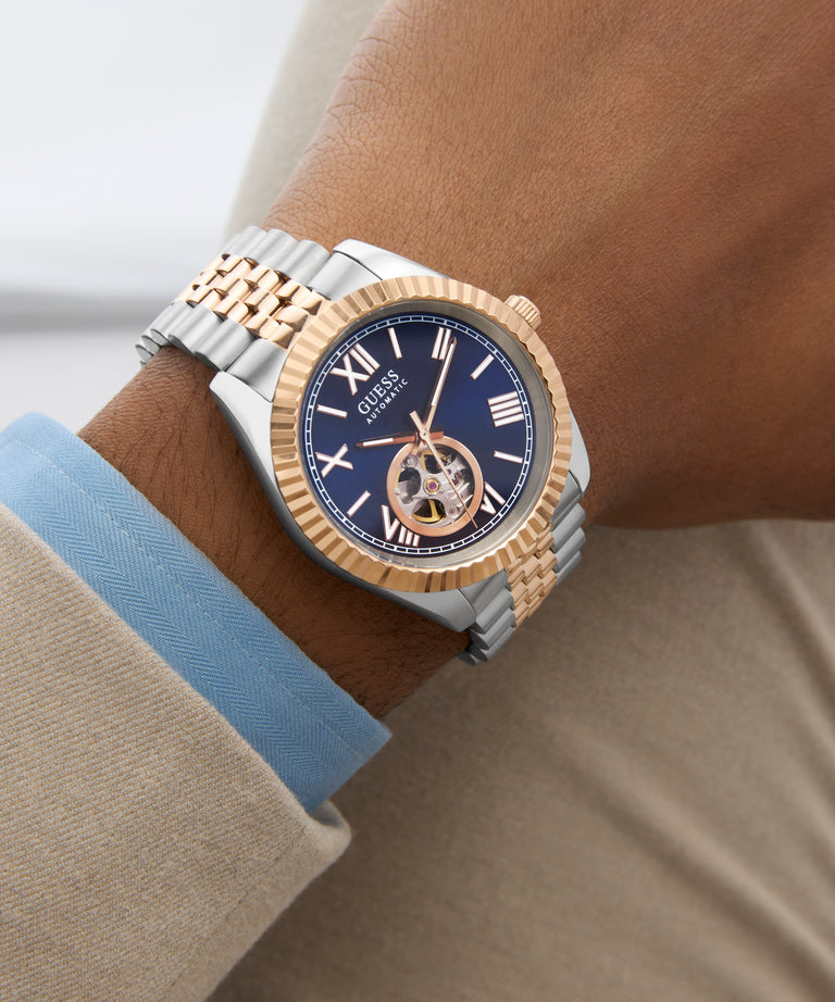 Close-up of a person wearing GUESS Mens 2-Tone Automatic Watch with a blue face.