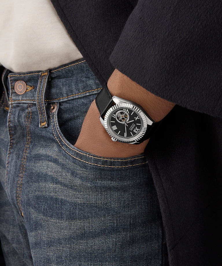 Person wearing a GUESS Mens Black Silver Tone Automatic Watch on a dark background
