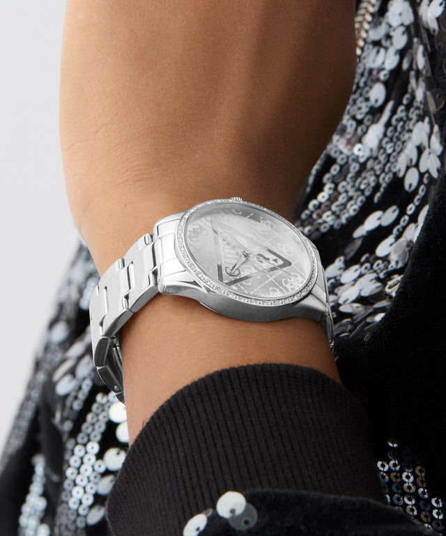 Silver watch on a wrist with a sequined garment in the background