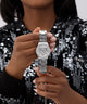 Person holding a silver GUESS Ladies Silver Tone Analog Watch with a triangle design, wearing a black sequin top.