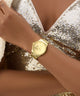 GUESS Ladies Gold Tone Analog Watch on a wrist with a sequined garment in the background