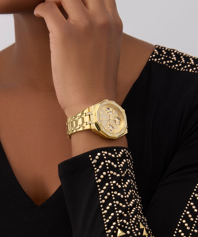 GUESS Ladies Gold Tone Multi-function Watch on a wrist with a black and gold patterned sleeve against a neutral background