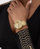 GUESS Ladies Gold Tone Multi-function Watch on a hand with black and gold embroidered sleeve