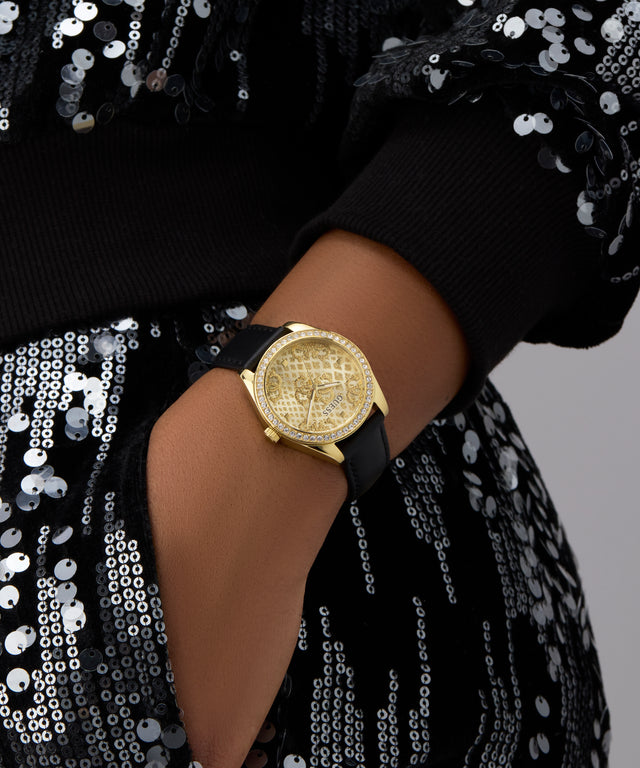 Gold GUESS Ladies Black Gold Tone Analog Watch on a wrist with a black strap against a sequined background