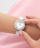 Silver heart-shaped GUESS Ladies Silver Tone Analog Watch with gemstones on a wrist against a pink background