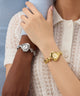 Two wrists wearing silver and gold watches with heart designs.
