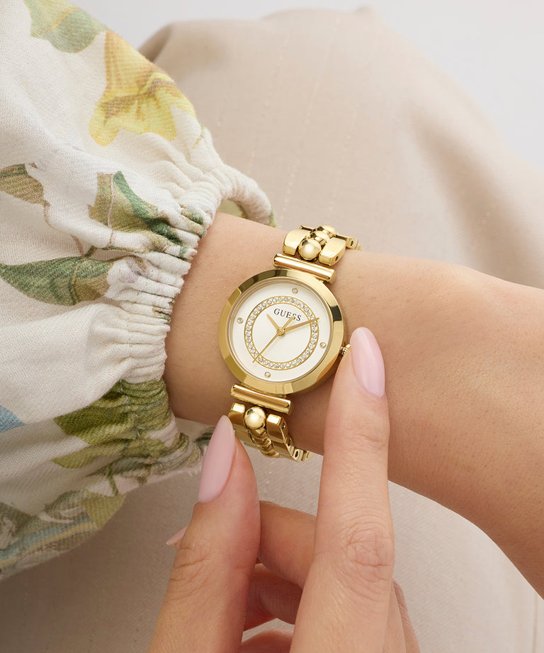 Gold GUESS Ladies Gold Tone Analog Watch on a wrist with a floral-patterned fabric background