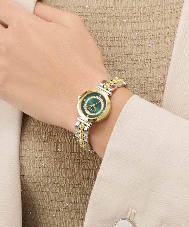 Gold and silver GUESS Ladies 2-Tone Analog Watch on a wrist with a textured beige background