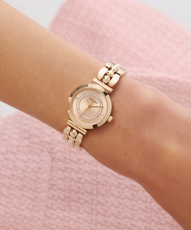 GUESS Ladies Rose Gold Tone Analog Watch on a wrist with a pink textured background