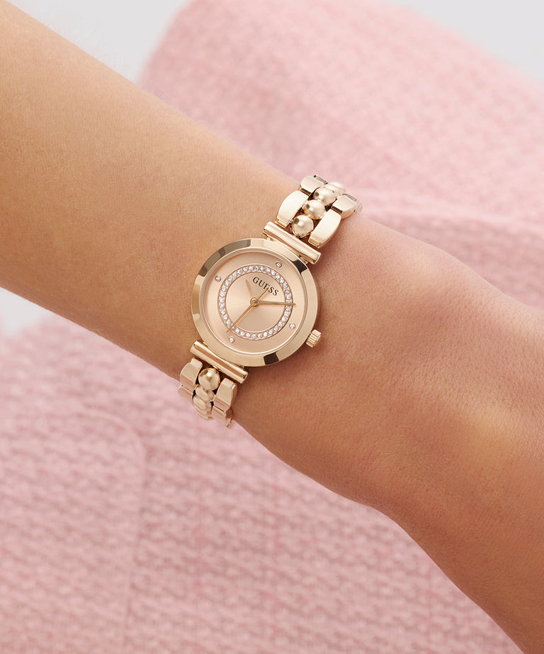 GUESS Ladies Rose Gold Tone Analog Watch on a wrist with a pink textured background
