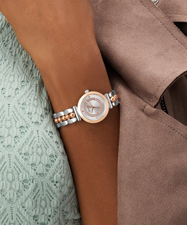 Silver and rose gold watch on a wrist with a brown coat and lace fabric background