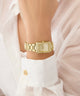 Gold GUESS Ladies Gold Tone Analog Watch on a person's wrist with a white outfit