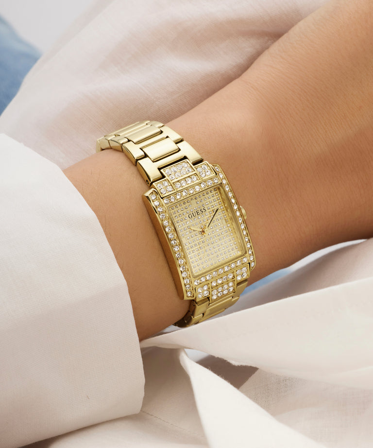 Gold GUESS Ladies Gold Tone Analog Watch with diamond accents on a wrist against a light background