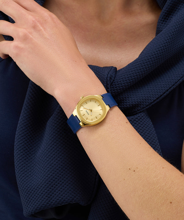 GUESS Ladies BLUE GOLD TONE Analog Watch with a blue strap on a person's wrist, wearing a navy blue garment.
