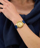 GUESS Ladies BLUE GOLD TONE Analog Watch with a blue strap on a person's wrist, wearing a navy blue garment.