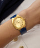 GUESS Ladies BLUE GOLD TONE Analog Watch with blue strap on a wrist against a neutral background