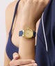 GUESS Ladies BLUE GOLD TONE Analog Watch with blue strap on a person's wrist against a neutral background