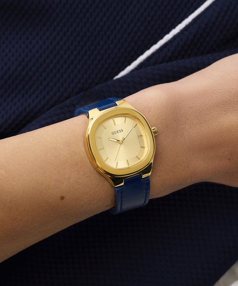 GUESS Ladies BLUE GOLD TONE Analog Watch with a blue strap on a wrist against a dark background