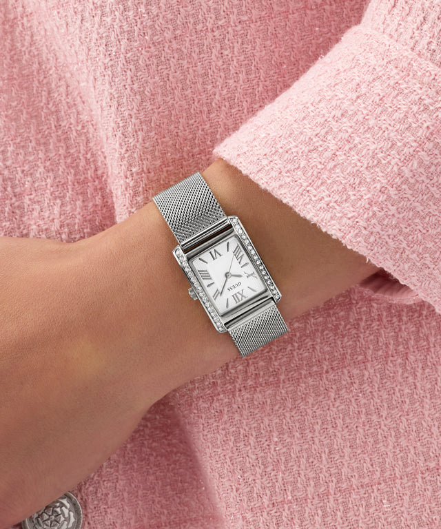 Silver GUESS Ladies Silver Tone Analog Watch on a wrist with a pink textured background