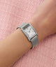 Silver GUESS Ladies Silver Tone Analog Watch with mesh band on a wrist against a pink textured background