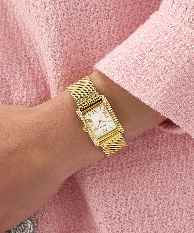 Gold GUESS Ladies Gold Tone Analog Watch on a wrist with a pink textured background