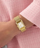 Gold GUESS Ladies Gold Tone Analog Watch on a wrist with a pink textured background