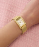 Gold GUESS Ladies Gold Tone Analog Watch on a wrist with a pink textured background