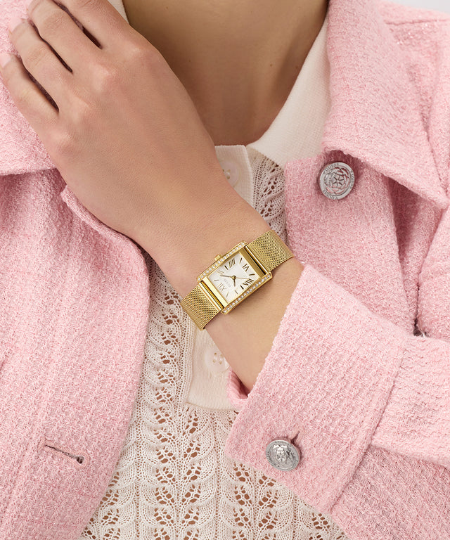 Gold GUESS Ladies Gold Tone Analog Watch on a wrist with a pink coat and lace top