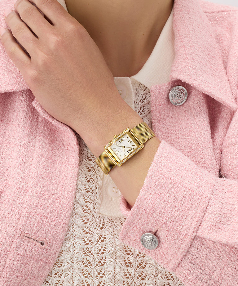 Gold GUESS Ladies Gold Tone Analog Watch on a wrist with a pink coat and lace top