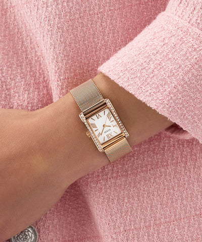 GUESS Ladies Rose Gold Tone Analog Watch on a wrist with a pink textured background