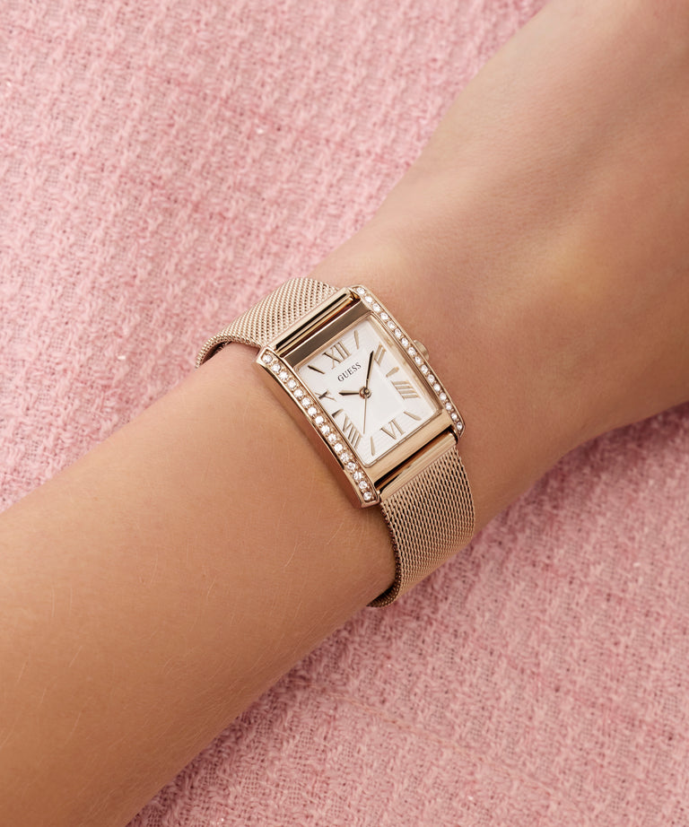 Rose gold watch on a wrist with a pink textured background