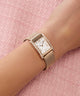 Rose gold watch on a wrist with a pink textured background
