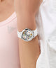 GUESS Ladies White Silver Tone Analog Watch with colorful accents on a wrist, wearing a light pink top and white pants.