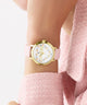 GUESS Ladies Pink Gold Tone Analog Watch with pink strap worn on a wrist, against a light background