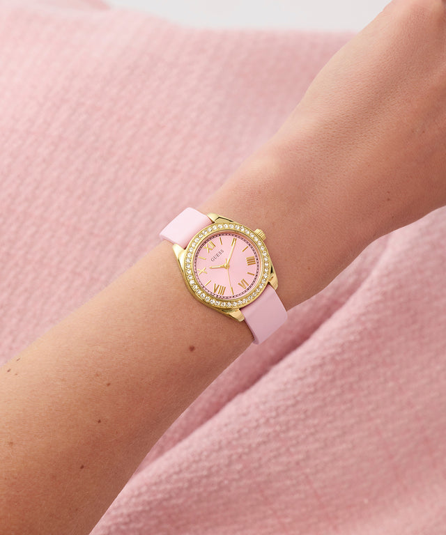 GUESS Ladies Mini Luna Pink Gold Tone Analog Watch with gold accents on a wrist against a pink background