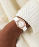 Rose gold watch with white strap on a wrist against a soft, light background