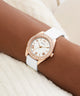 Rose gold watch with white strap on wrist against a neutral background