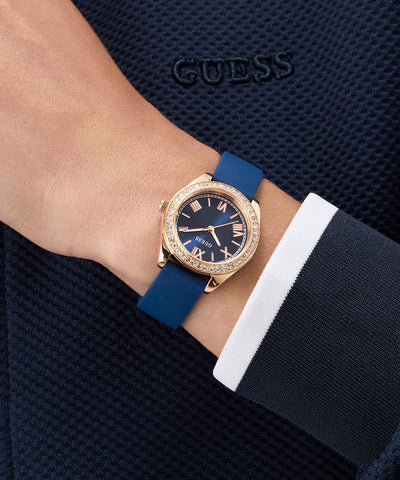 Person wearing a GUESS Ladies Mini Luna Blue Rose Gold Tone Analog Watch with a blue strap and rose gold case.