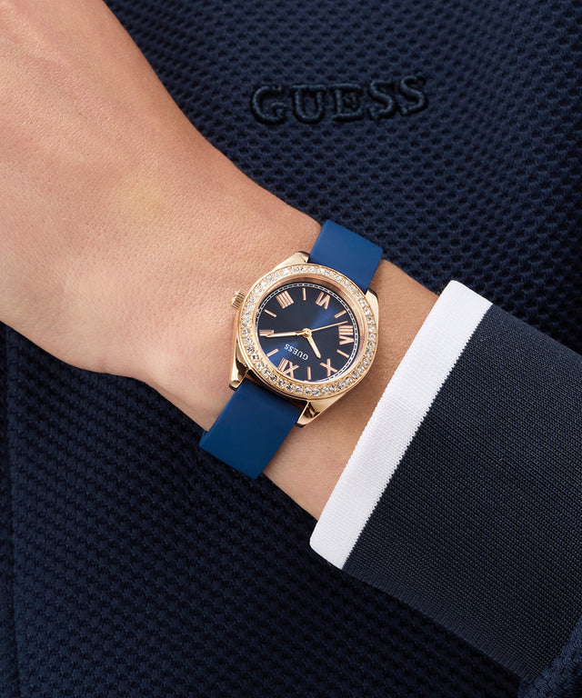 Person wearing a GUESS Ladies Mini Luna Blue Rose Gold Tone Analog Watch with a blue strap and rose gold case.