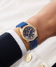 Wrist wearing a blue and gold watch with a white background